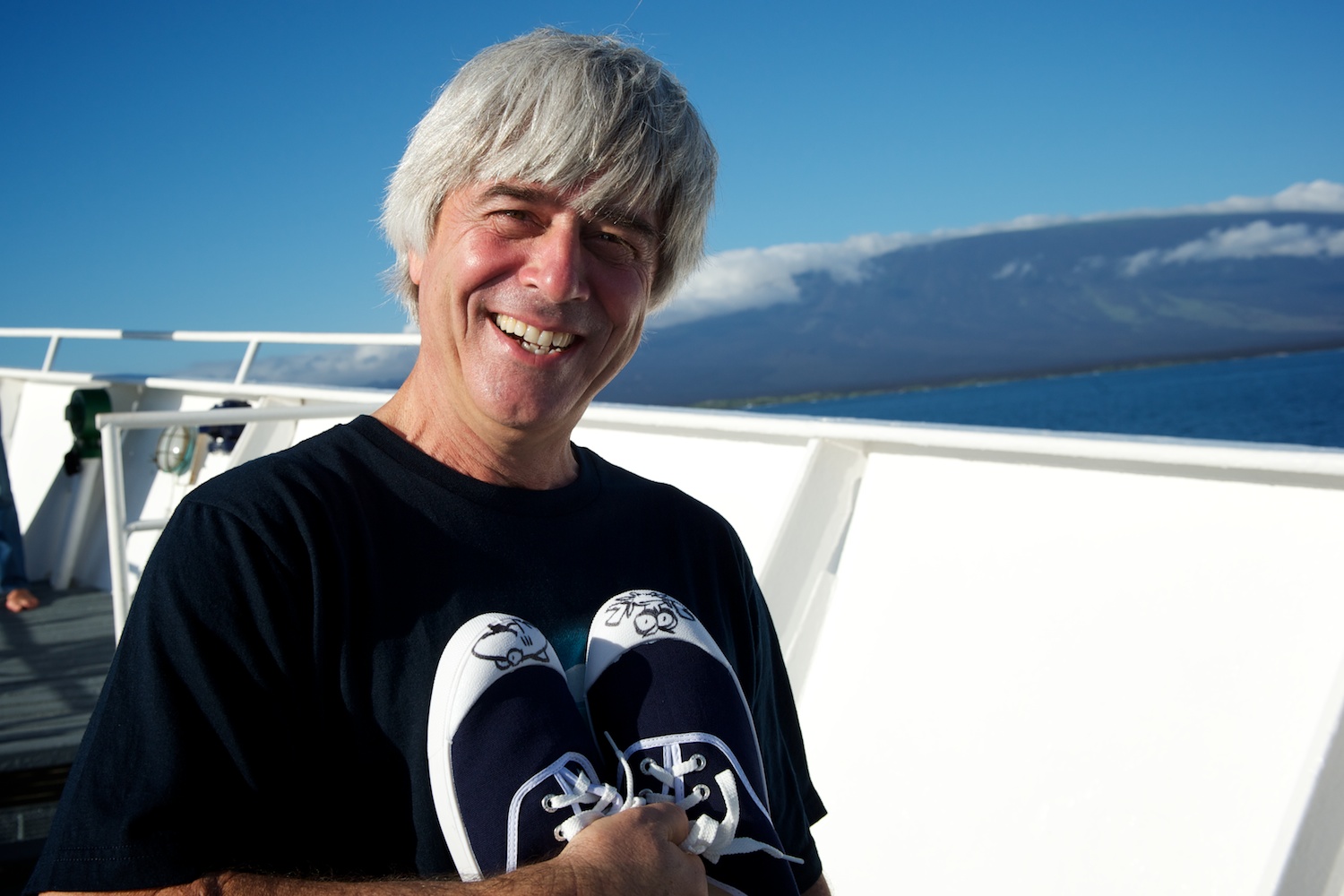 Mike deGruy holds a pair of tennis shoes decorated by Jim Toomey of "Sherman's Lagoon," aboard the Mission Blue Voyage to the Galápagos. Courtesy James Duncan Davidson.