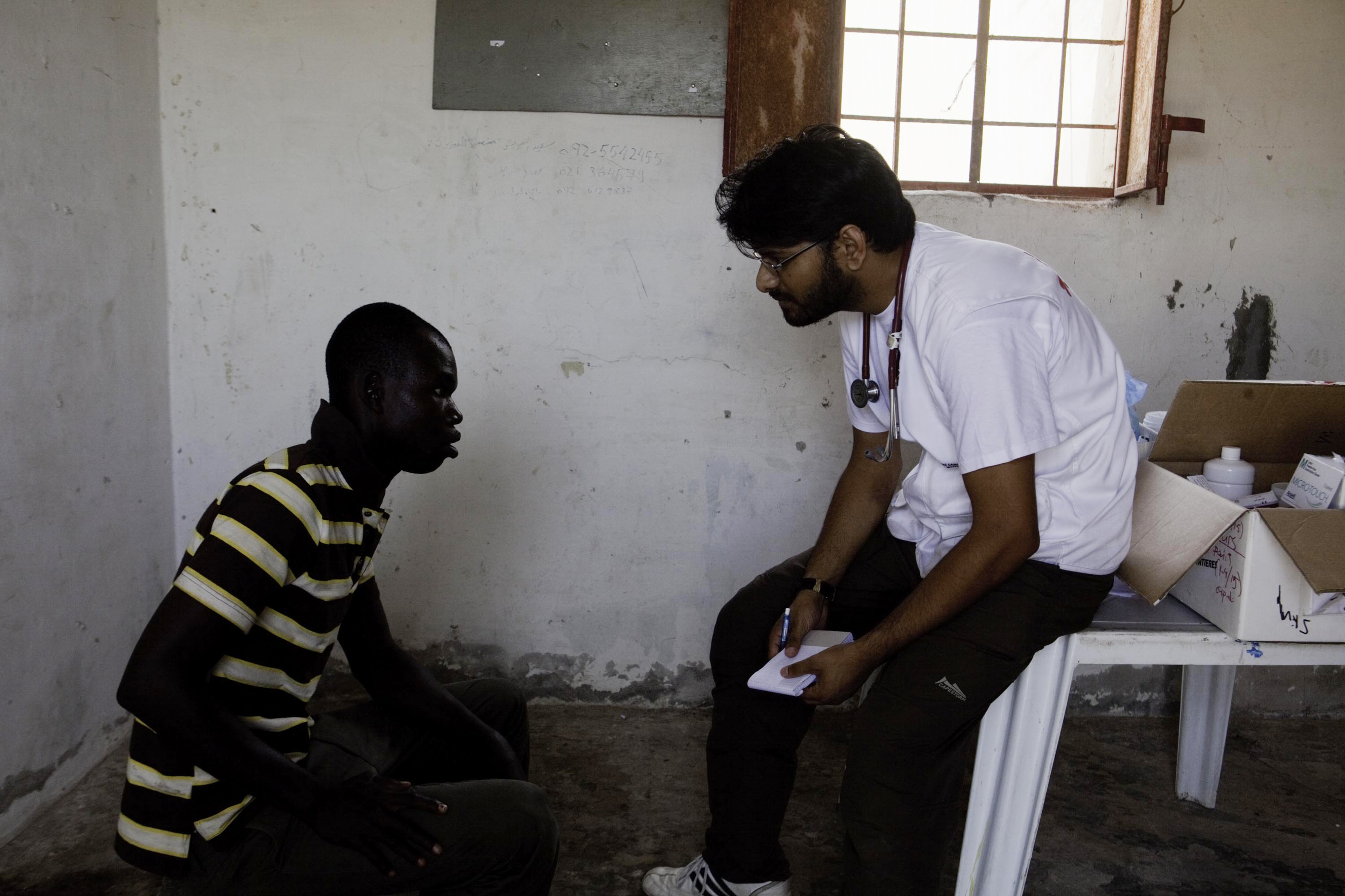 Mohammed Dalwai provides a medical consultation to one of the 800–1000 migrants and refugees living amongst boats on an abandoned military base on the outskirts of Tripoli. Photo: MSF