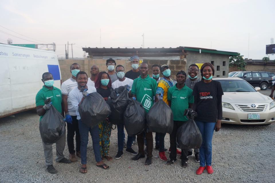 A group of volunteers stand together holding full trash bags and smiling.