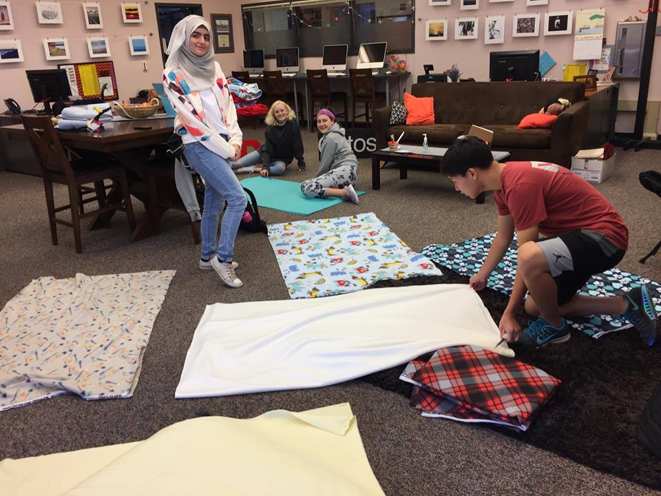 A young woman stands amid laid out blankets in a room, as a man lays another out.